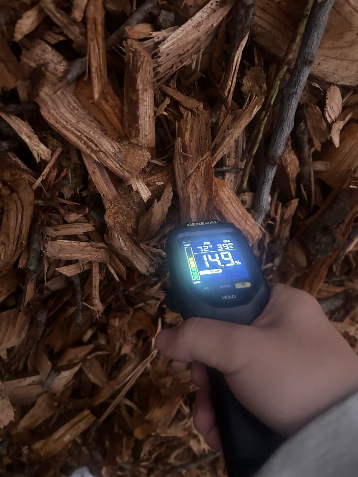 Handheld moisture meter reading almond wood chips in the field